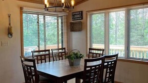 Zona pranzo con tavolo e sedie in legno, un lampadario e ampie finestre con tende.