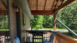 Una terrazza in legno coperta con due sedie blu e un tavolo, circondata da una ringhiera in legno.