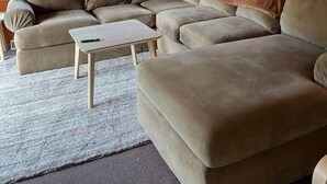 Un accogliente soggiorno con un divano componibile, un tavolino, una sveglia e un quadro appeso al muro.
