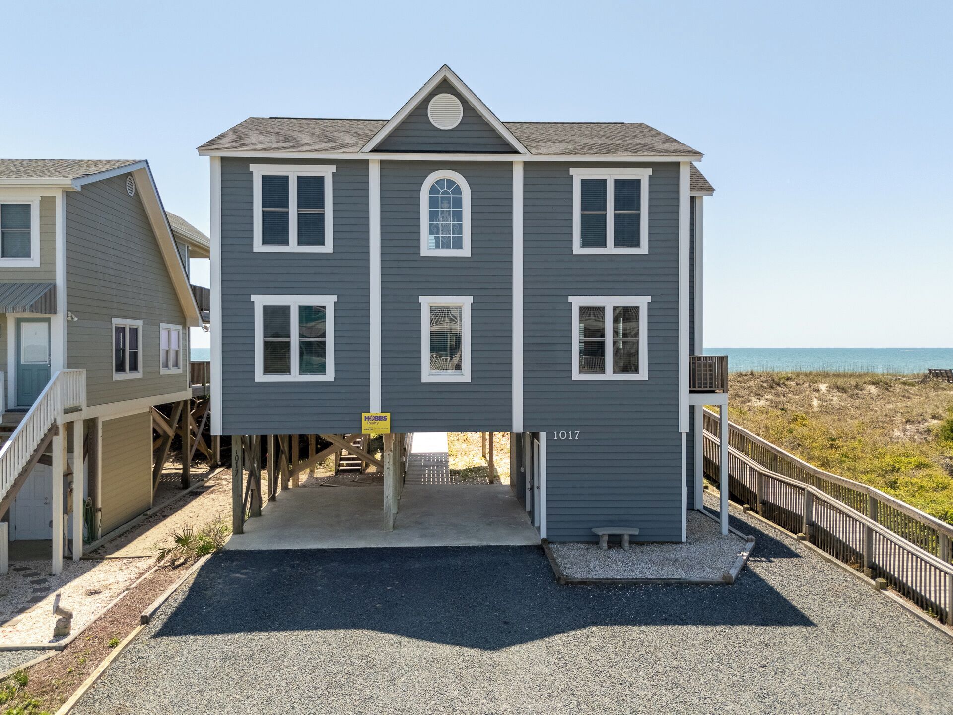 A two-story house with a front porch, a small deck, and a beach view.