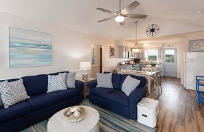 A living room with a sofa, a coffee table, and a kitchen in the background. - Relax at Blue Crab Shack, a spacious dog-friendly home with marsh views in Holden Beach. (Holden Beach)
