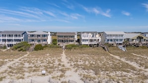 A beachfront property with multiple multi-story buildings, sandy beach in the foreground, and a clear sky. - Dolphin's Watch: A stunning oceanfront 4BR retreat in Supply, NC, perfect for 10 guests. (Supply)
