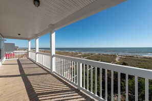 Eine überdachte Holzterrasse mit weißen Geländern mit Blick auf einen Strand.