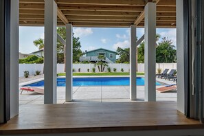 Blick auf einen Poolbereich mit überdachter Terrasse, ein Haus im Hintergrund und einem weißen Zaun.