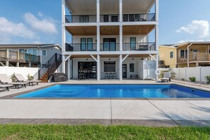 A two-story building with a pool, outdoor seating, and a covered patio area. - Sunset Skies: Stylish 4BR beach home in Holden Beach with a private pool. (Holden Beach)