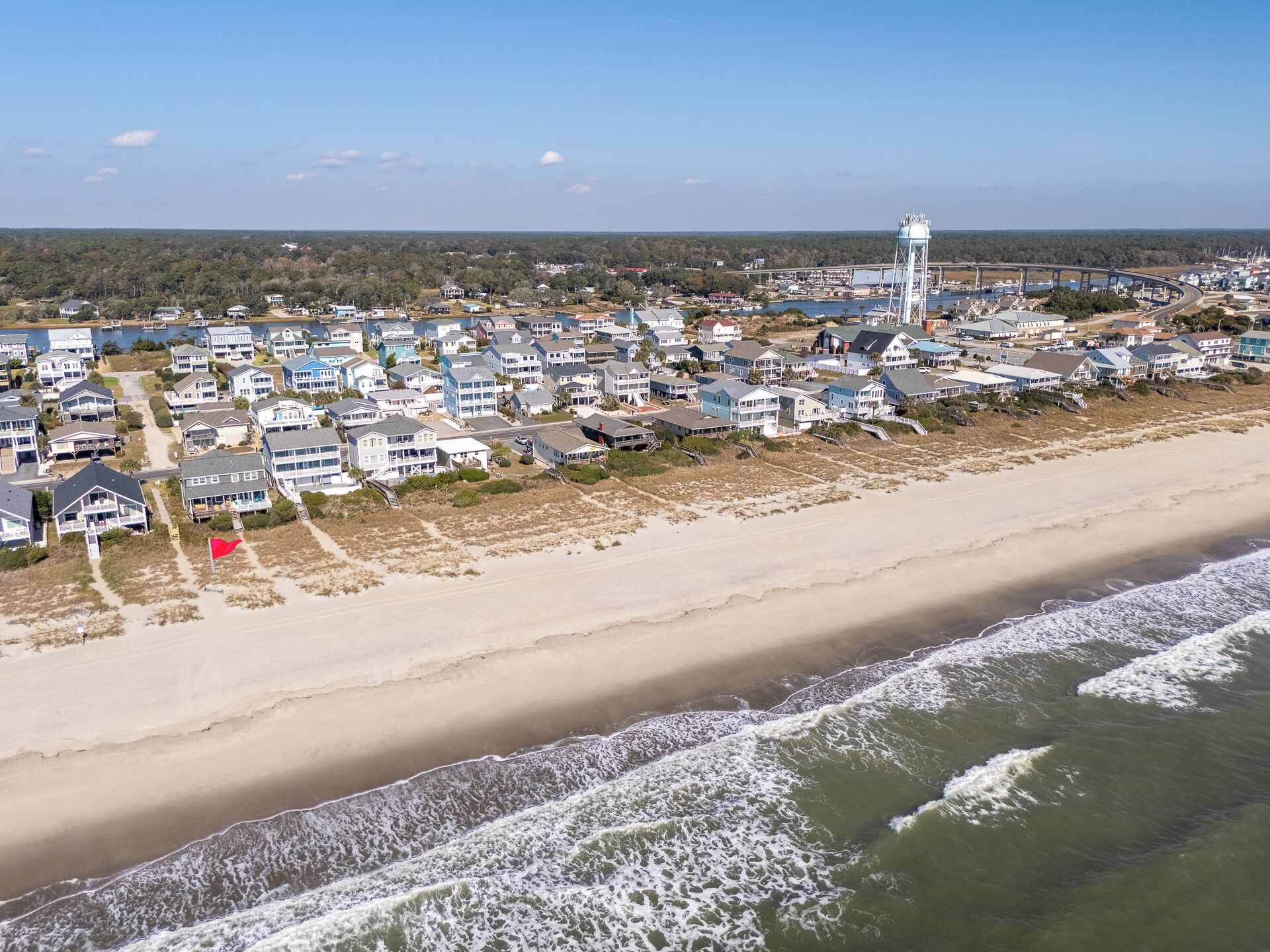 A coastal town with beachfront properties, a water tower, and a bridge in the background.