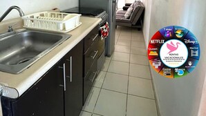 Une cuisine compacte équipée d’un évier, d’une cuisinière et d’un réfrigérateur. On y trouve également un petit coin repas avec une chaise et une table.
