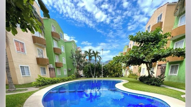 Une piscine entourée d’immeubles à plusieurs étages dotés de balcons, sous un ciel dégagé.