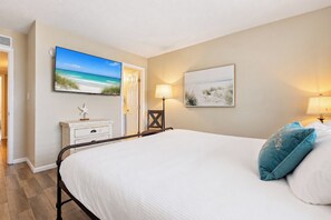 A bedroom with a bed, a nightstand, a television, and two wall-mounted lamps. - Beach Escape • Pool View • Walk to Beach + Food (Fort Walton Beach)