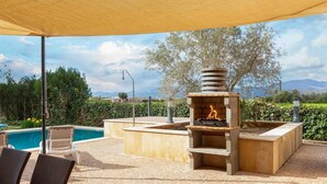 Um pátio externo com piso de ladrilho, churrasqueira embutida, cadeiras de vime, piscina e vista para montanhas.
