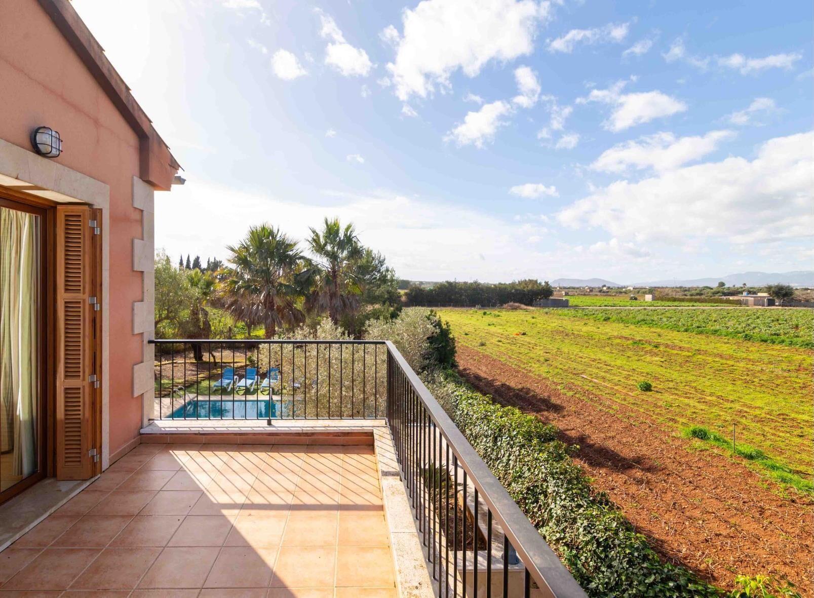 Un balcon avec une piscine, une vue sur un champ verdoyant et un ciel dégagé.