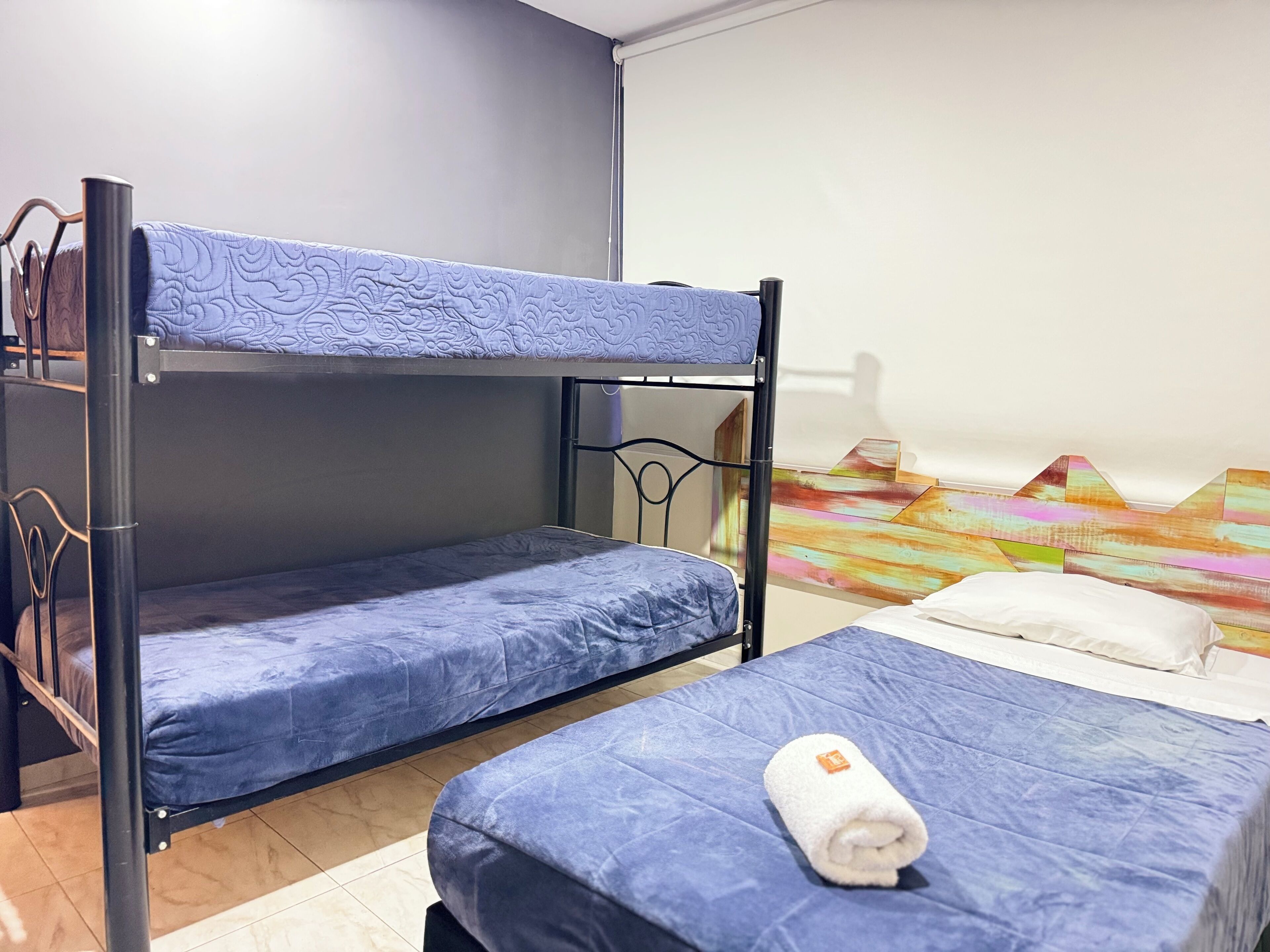 Un letto a castello con materasso blu, un tavolino con un asciugamano arrotolato e una decorazione vivace al muro.