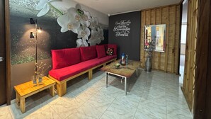 A room with a red sofa, a small wooden table, a wall with an orchid mural, and a sign with a family welcome message. - Tu Hotel Chía (Chía)