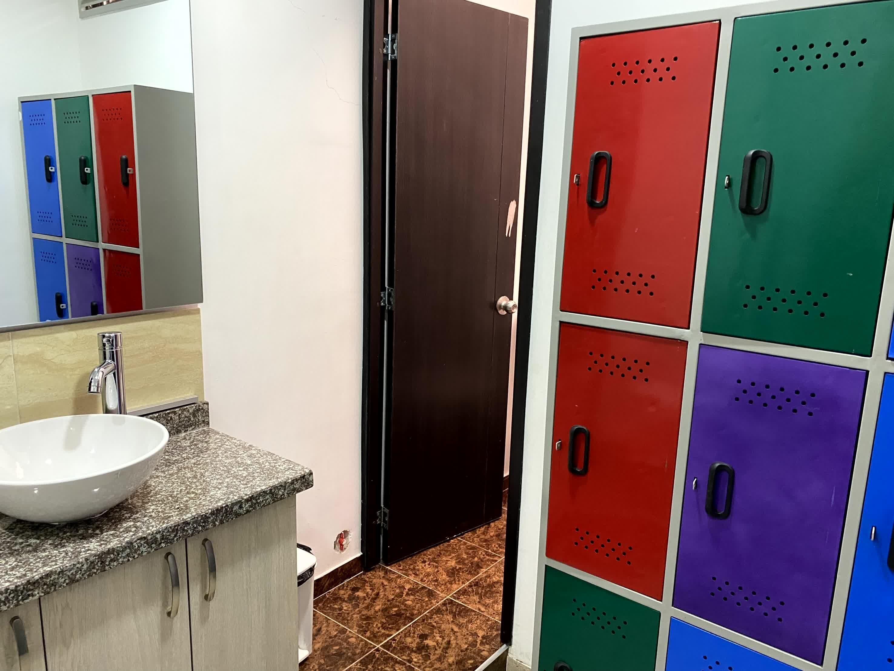 Een badkamer met een witte wastafel, een spiegel en een wandkastje. Er zijn kasten in rood, groen, blauw en paars.