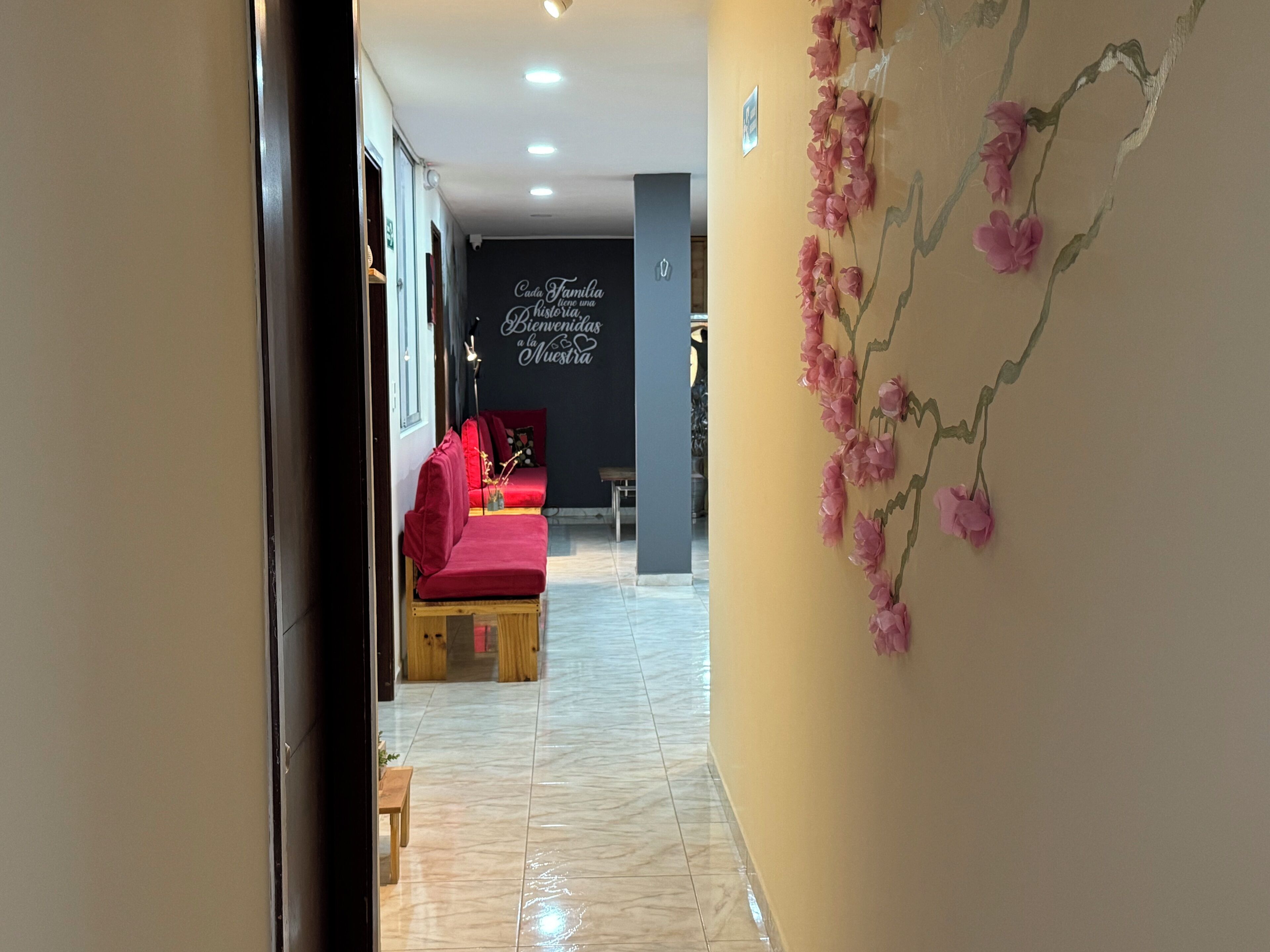 Un couloir avec un canapé rouge, un mur orné d’un motif floral et un panneau indiquant : « Bienvenue à nos invités ».