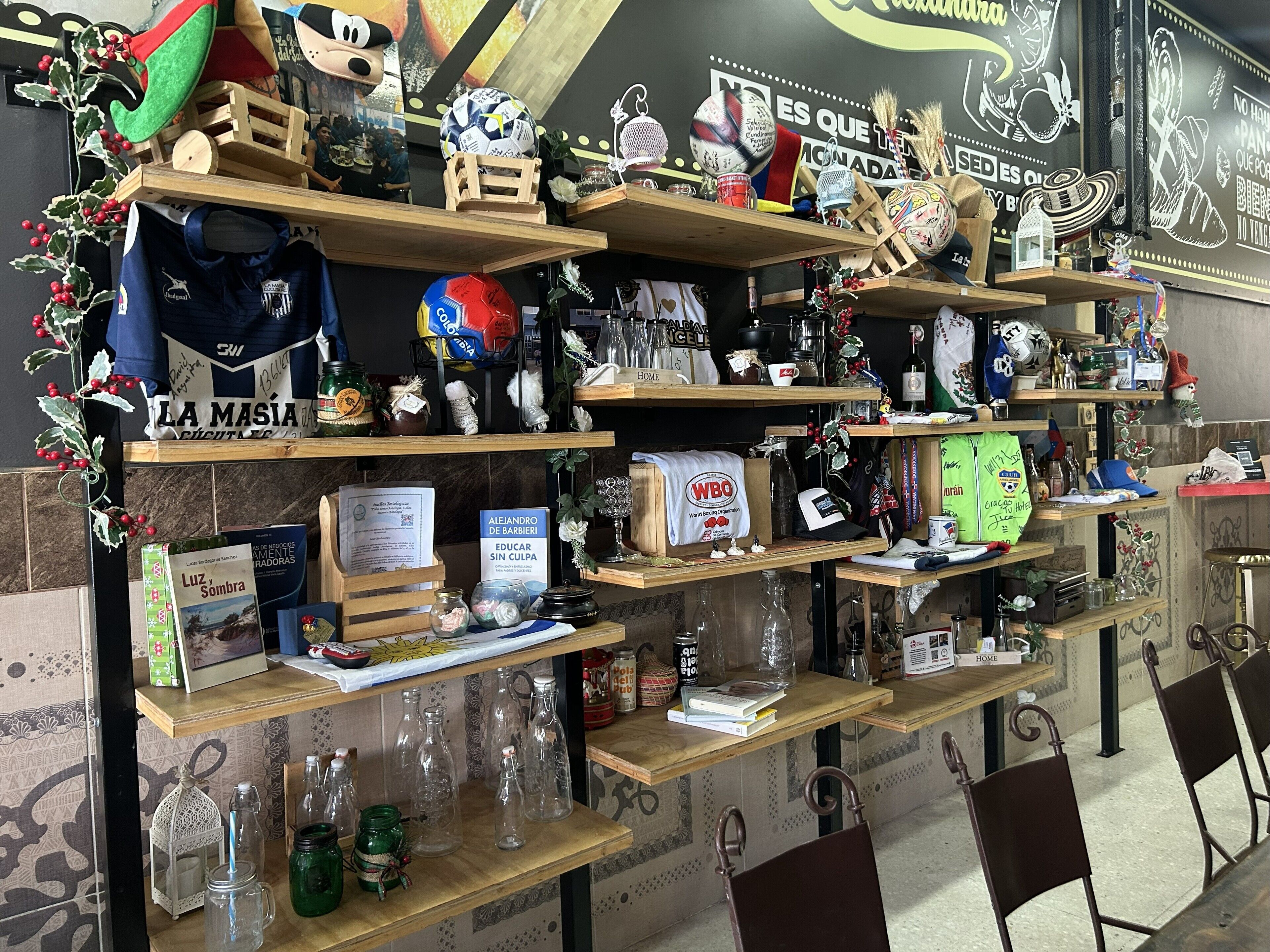 Une présentation soignée d’objets de collection et de souvenirs liés au sport, notamment des ballons de football, des maillots et divers petits articles, disposés sur des étagères en bois.