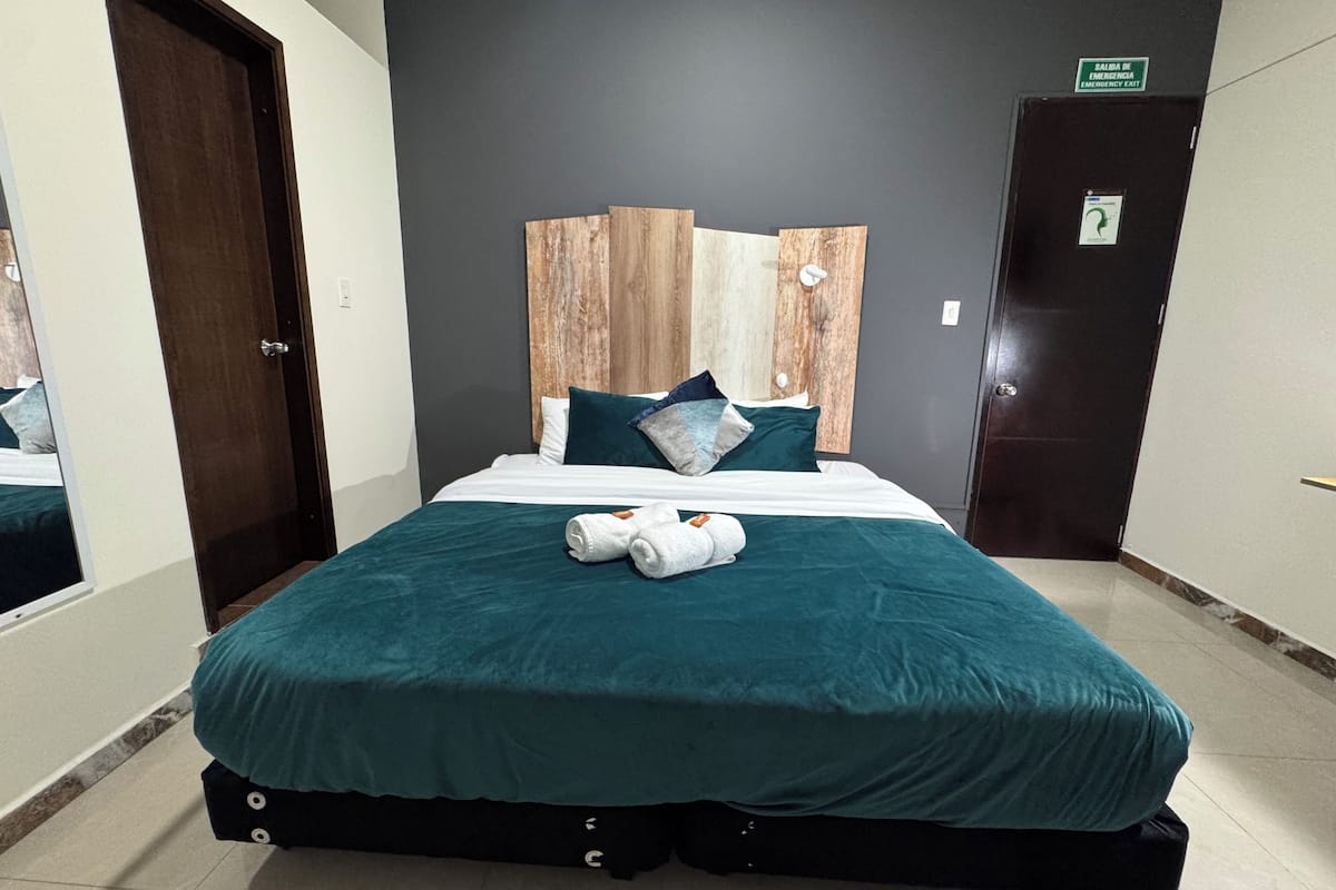 Une chambre d’hôtel avec un lit, une tête de lit, une porte et un panneau indiquant la sortie de secours.