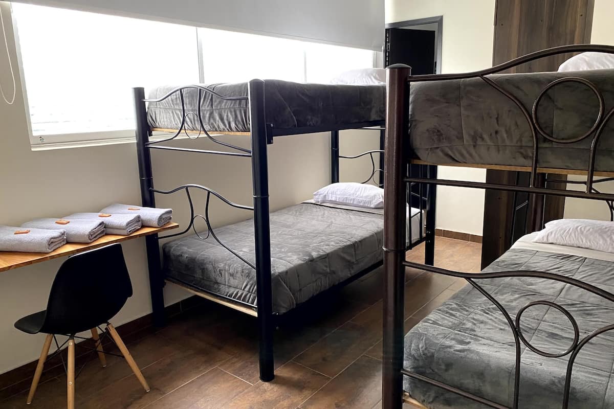 Une chambre avec un lit superposé, un bureau et une chaise, une fenêtre et une porte.