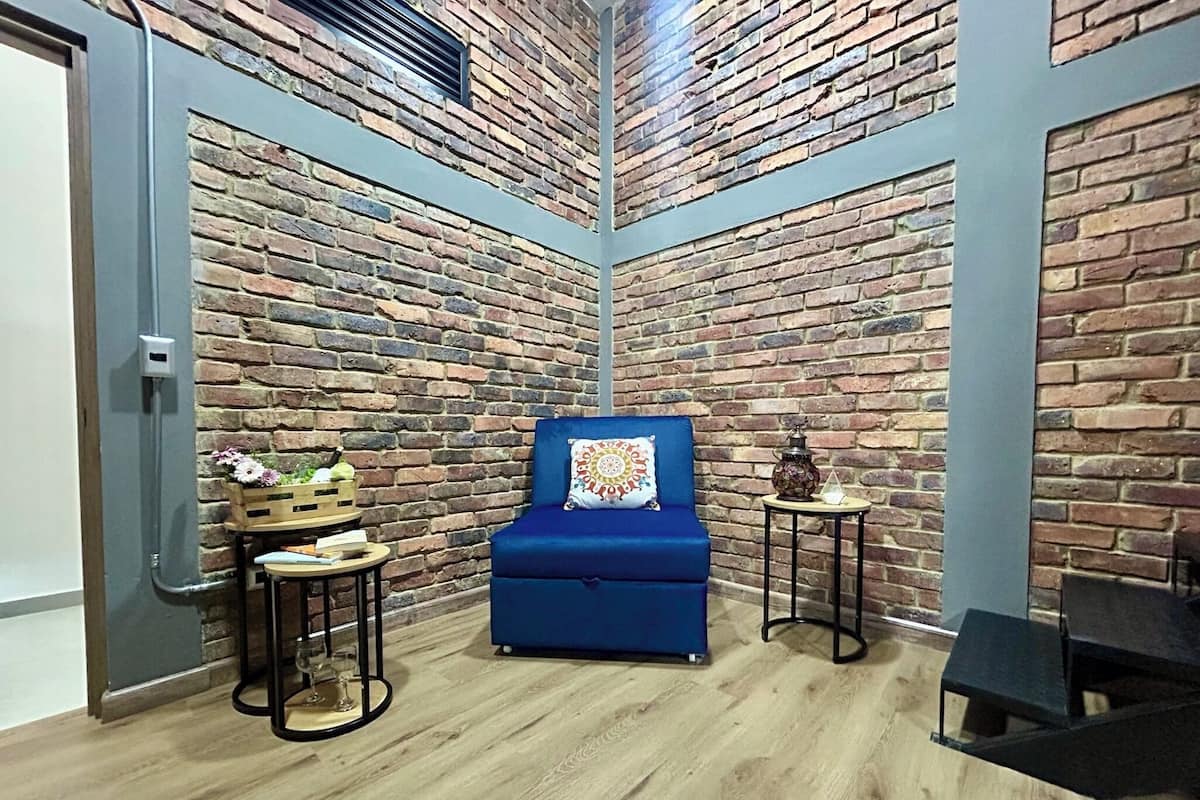 Une pièce chaleureuse avec un canapé bleu, une petite table en bois sur laquelle est posée une lanterne, et un mur en briques.