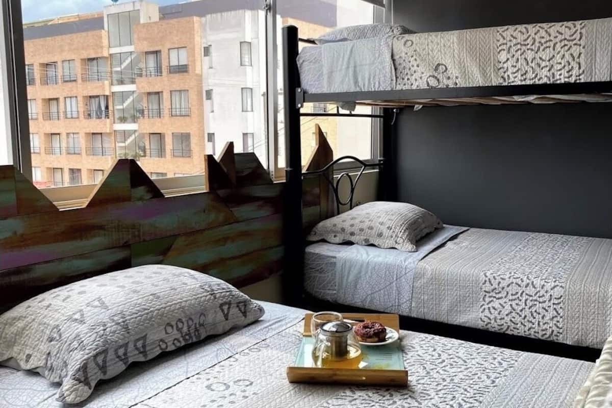 Une chambre de dortoir avec des lits superposés, une fenêtre donnant sur des immeubles et un plateau avec une boisson et un beignet posé sur le lit.