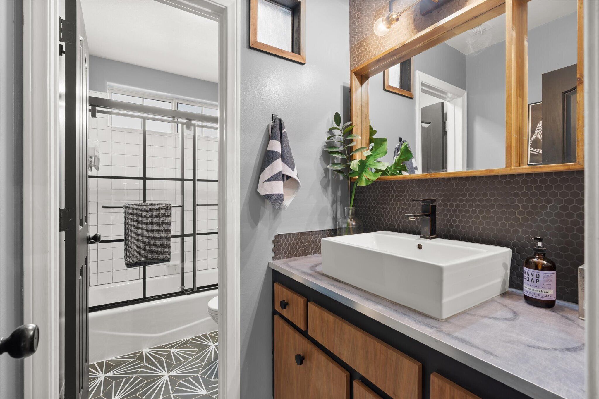 A modern bathroom with a white bathtub, a large mirror, and a wooden vanity with a white sink.