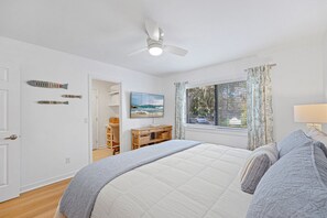 Ein Schlafzimmer mit einem Bett, einem Deckenventilator, einem Fenster mit Vorhängen und Blick ins Freie.