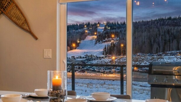 Ein Essbereich mit Tisch für vier Personen, einer Kerzenarragement und Blick auf eine verschneite Landschaft durch große Fenster.