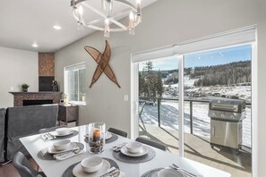 A dining area with a table set for six, a fireplace, and a large window with a view of a snowy landscape. - Brian Head Retreat - Walk to Lifts/Family Friendly/Spacious/Modern (Brian Head)