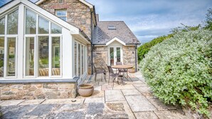 A stone house with a large glass window, a patio with outdoor furniture, and a hedge. - Craig y Mor, Holiday Cottage Newport, Sleeps 10, 5 bedrooms,  bathrooms (Newport)