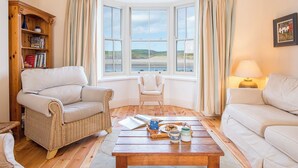 A cozy living room with a large bay window, wicker furniture, and a wooden coffee table. - Craig y Mor, Holiday Cottage Newport, Sleeps 10, 5 bedrooms,  bathrooms (Newport)