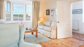 A cozy living room with a sofa, a table, and a view of the outdoors through large windows. - Craig y Mor, Holiday Cottage Newport, Sleeps 10, 5 bedrooms,  bathrooms (Newport)