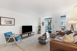 A modern living room with a flat-screen TV, a blue armchair, a brown sofa, and a coffee table. - Old Town Paradise with Pool - Mid Century Condo, one dog welcome! (Scottsdale)