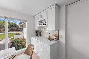 A modern kitchen with white cabinetry, a built-in wine rack, and a view of a garden through a sliding glass door. - Charming 4-bedroom house in tranquil Sanibel with private beach access! (Sanibel)