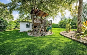 A treehouse with a wooden structure and a slide, surrounded by lush greenery. - el laguito (Miami)