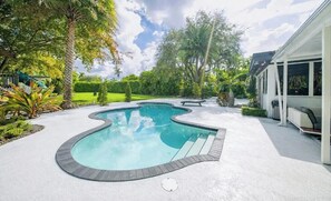 A swimming pool with a unique shape, surrounded by a concrete deck and lush greenery. - el laguito (Miami)