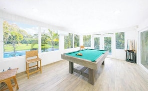 A pool table in a bright room with large windows and a view of a garden. - el laguito (Miami)