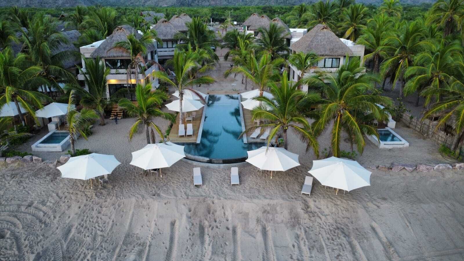 A resort with a central swimming pool, multiple thatched-roof buildings, and palm trees.