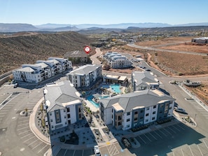 A multi-story residential building complex with a central courtyard, parking, and a view of the surrounding landscape. - Resort Condo with Lazy River & Pools (Hurricane)