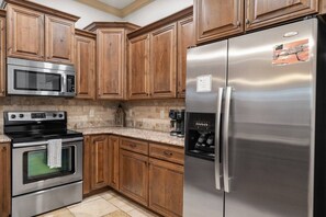A kitchen with wooden cabinets, stainless steel appliances including a refrigerator, microwave, and oven, and a coffee maker on the countertop. - Resort Condo with Lazy River & Pools (Hurricane)
