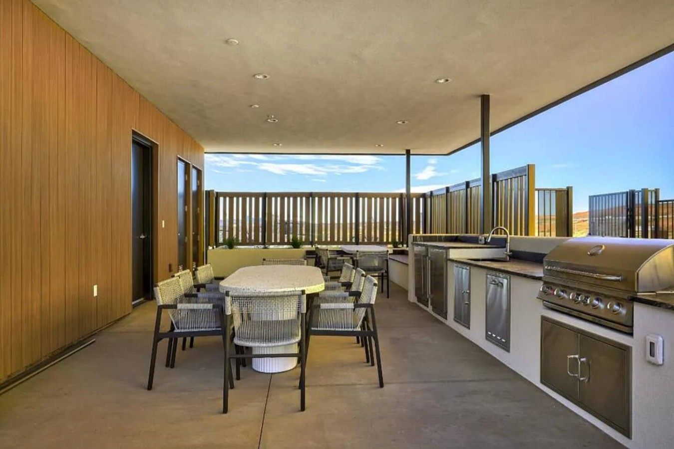 An outdoor patio with a dining table and chairs, a grill, and a view of the landscape.