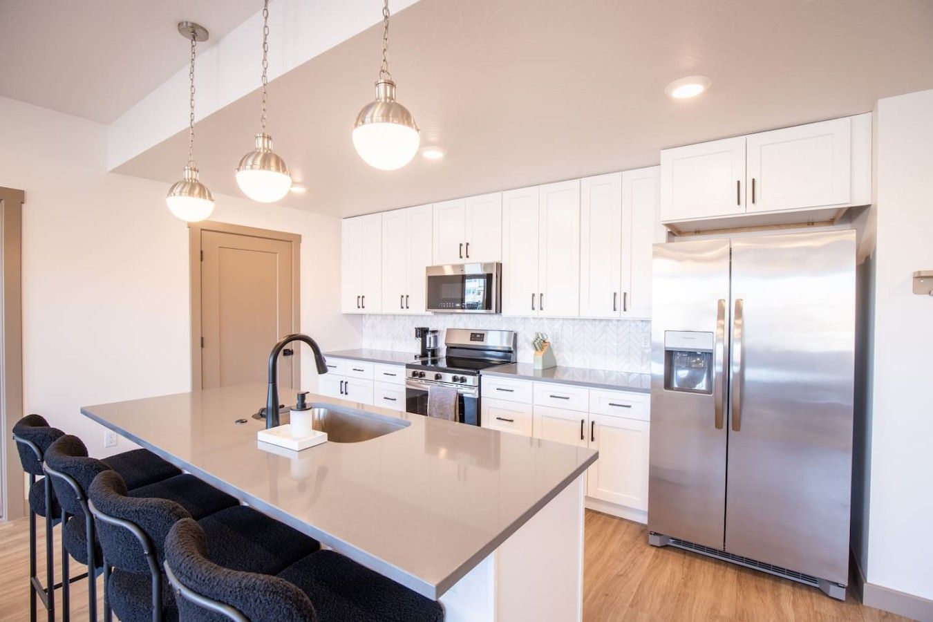 A modern kitchen with white cabinets, stainless steel appliances, and pendant lighting.
