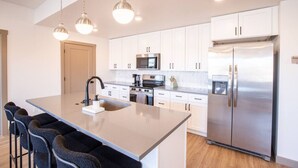 Una cocina moderna con armarios blancos, un refrigerador de acero inoxidable, horno empotrado y una isla grande con taburetes de bar.