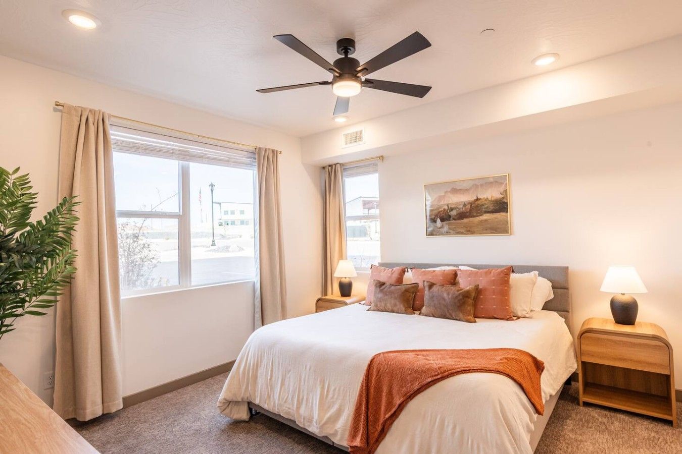A bedroom with a bed, two bedside tables, a ceiling fan, and a window with curtains.