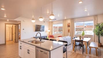 Une cuisine moderne avec un îlot central, un coin repas comprenant une table et des chaises, un canapé et un téléviseur fixé au mur.