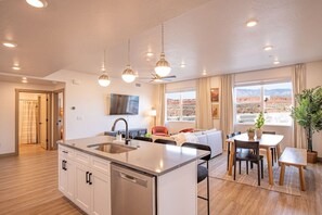 Een moderne keuken met een centraal eiland, een zithoek met een tafel en stoelen, een bank en een aan de muur bevestigde televisie.