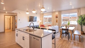 Una cocina moderna con una isla central, una zona de comedor con mesa y sillas, un sofá y un televisor montado en la pared.