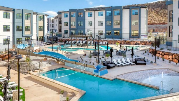 Un resort con varias piscinas, un tobogán de agua, sillas de descanso y montañas al fondo.