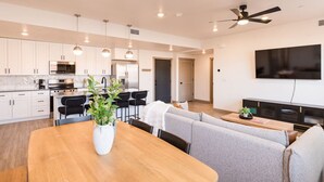 Una cocina moderna con armarios blancos, una mesa de comedor con sillas, un televisor montado en la pared y un ventilador de techo.