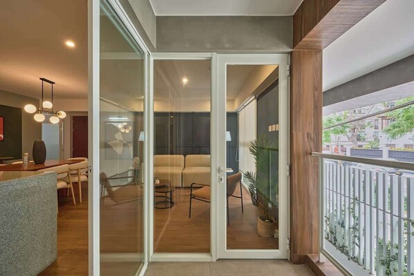 Ein modernes Interieur mit einer Glastür, die in einen Wohnbereich führt, einem Essbereich mit Tisch und Stühlen sowie einem Balkon mit Geländer.