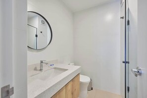 Ein modernes Badezimmer mit rundem Spiegel, Waschbecken, Toilette und Duschabtür aus Glas.
